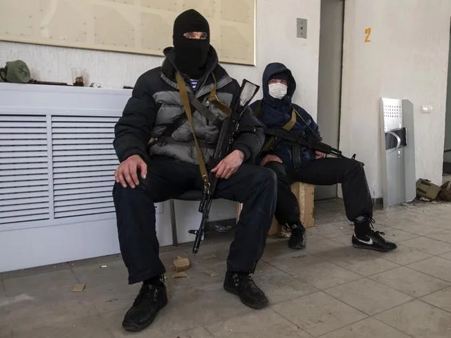 Неизвестные с автоматами охраняют захваченное здание СБУ в Луганске. В этих людях заметна военная выправка. Фото Рейтер.