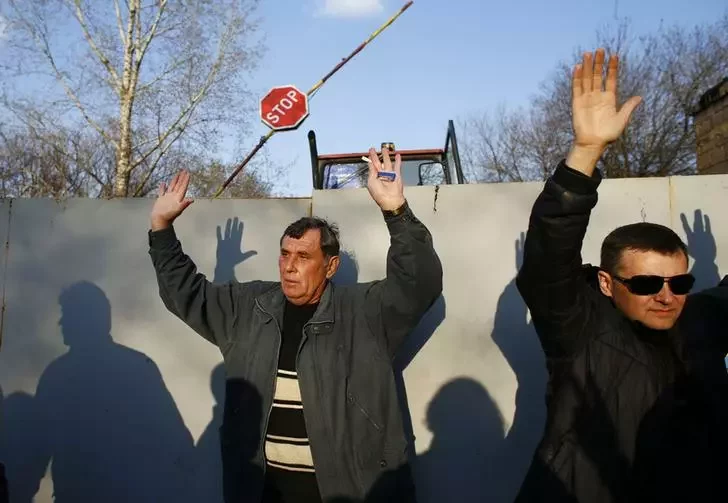 Прарасійскія актывісты стаяць з паднятымі ўверх рукамі на аэрадроме ў Краматорску.