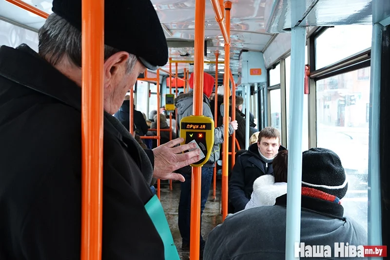 Мужчина знакомится с новым устройством, прикладывая талончик на проезд к валидатору в минском трамвае.