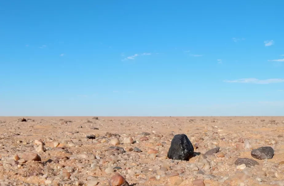 Сярод астатніх камянёў у пустыні, аскепак метэарыта выдзяляецца сваім насычаным чорным колерам. Фота: PETER JENNISKENS.