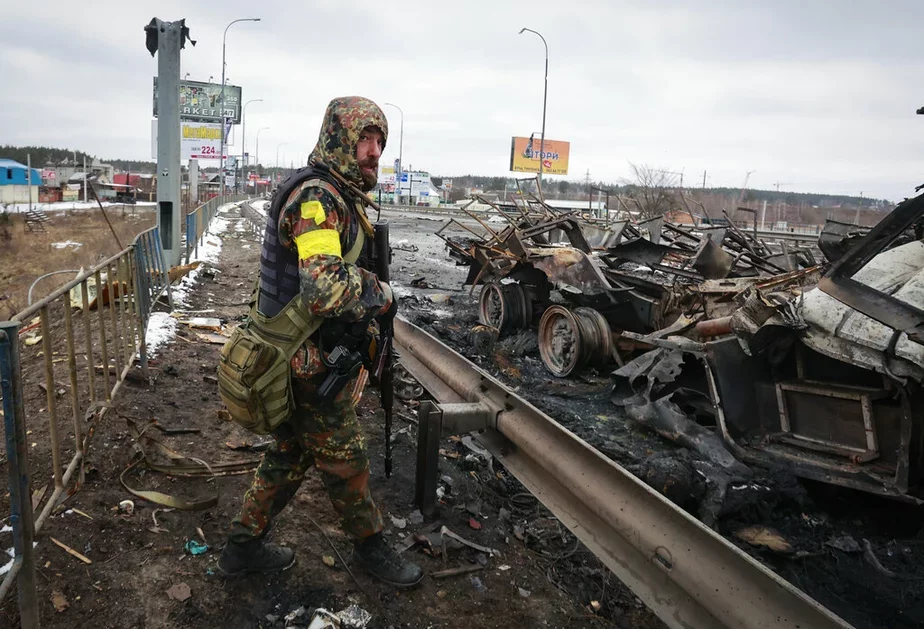 Вооруженный мужчина стоит возле остатков российской военной колонны, город Буча недалеко от Киева, 1 марта. Источник: АР.