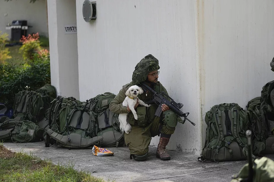 Израильский солдат держит собаку в кибуце Кфар-Аза во вторник, 10 октября 2023 года. Боевики ХАМАС захватили Кфар-Азу в субботу, где многие израильтяне были убиты и взяты в плен. Фото: AP Photo / Erik Marmor 
